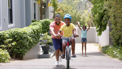 Padre-Afroamericano-Enseñando-A-Su-Hijo-A-Andar-En-Bicicleta,-Madre-Y-Hermana-Animando,-Cámara-Lenta