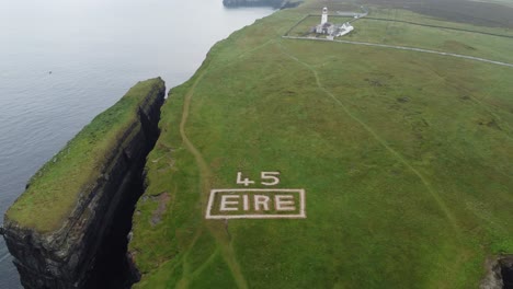 Drone-moving-up-from-WW2-marker-revealing-the-lighthouse-at-Loop-Head-peninsula