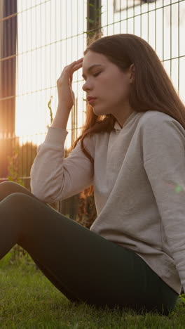 una mujer deprimida descansa en la hierba cerca del estadio. enfrentando desafíos emocionales de aislamiento y frustración mientras el sol se pone echando un tono melancólico sobre la escena