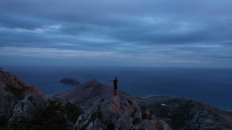 young man stretches out arm on top of mountain in porto santo, madeira