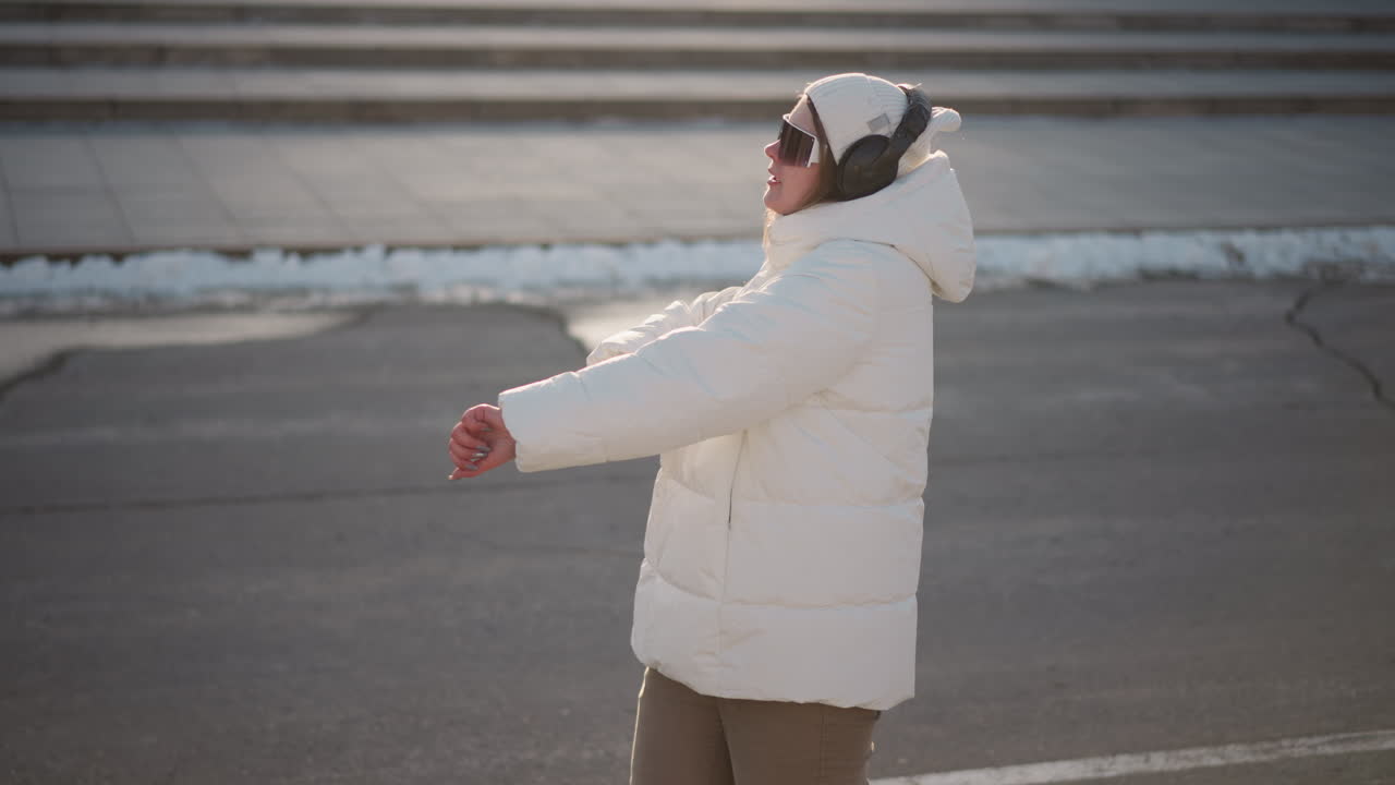 Character expressing herself as she moves her hands while spinning in park, wearing white puffy coat and beanie under winter sun, joyful vibe flowing through expressive gesture and natural smile