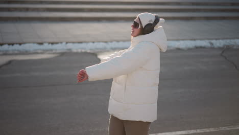 character expressing herself as she moves her hands while spinning in park, wearing white puffy coat and beanie under winter sun, joyful vibe flowing through expressive gesture and natural smile