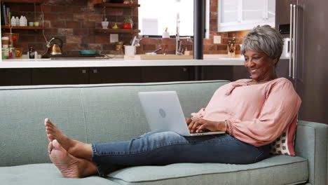 senior woman relaxing on sofa at home using laptop to shop online