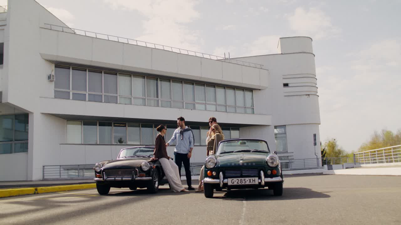 Friends Posing with Vintage Cars in Front of Modern Building
