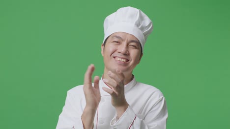 녹색 스크린 배경 스튜디오에 서 있는 동안 미소 짓고 손을 치는 아시아 남자 셰프의 클로즈업