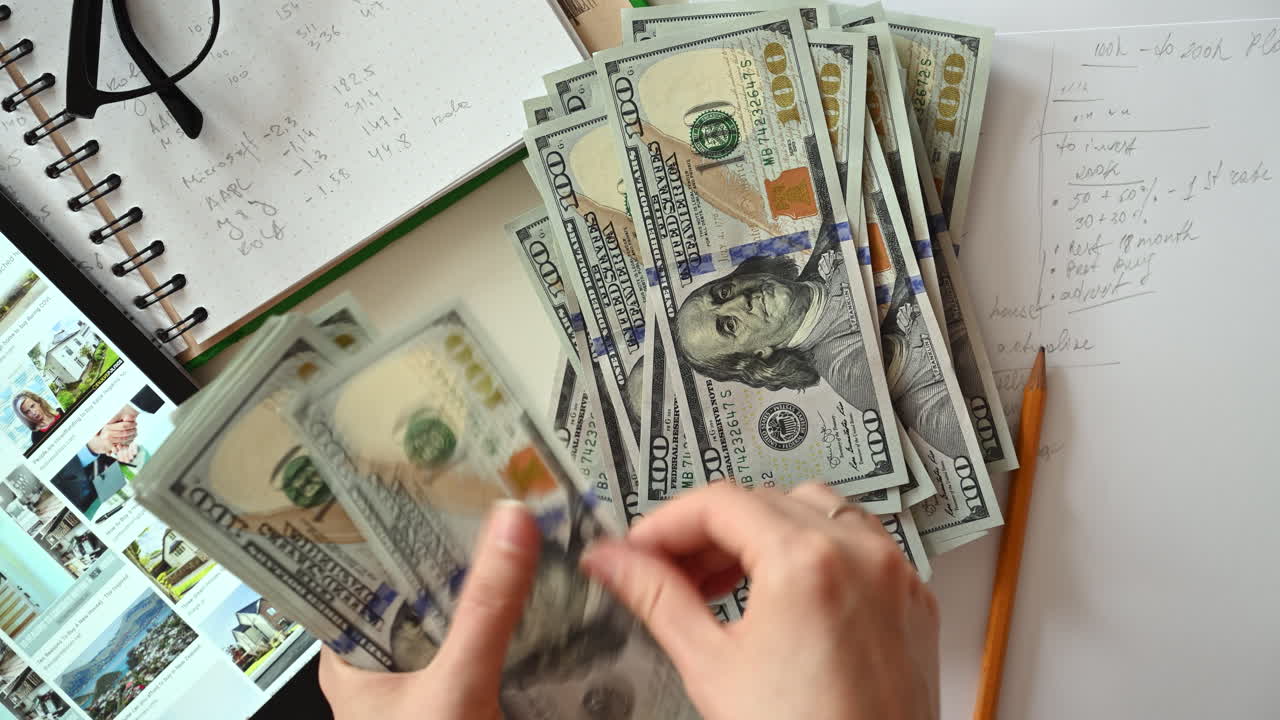 Close up of hands fanning out dollar bills on a desk with notes and a tablet