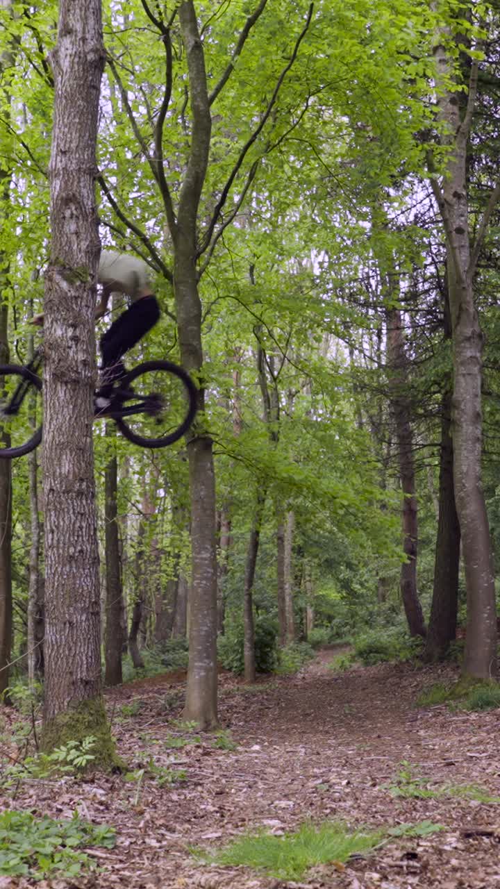 Drone Vertical Video Tracking Man On Mountain Bike Cycling Doing Mid-Air Jump On Trail Through Woodland 4