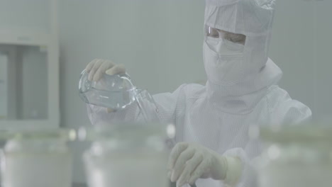 male scientist or researcher transferring solution samples to a tissue culture flask for cell culture assay in biological cabinet on in cleanroom environmental facility laboratory.