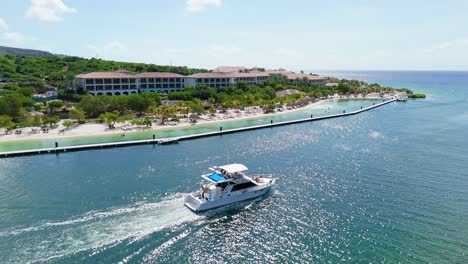 drone follows large speed boat yacht driving in front of beach front resort in caribbean at santa barbara beach