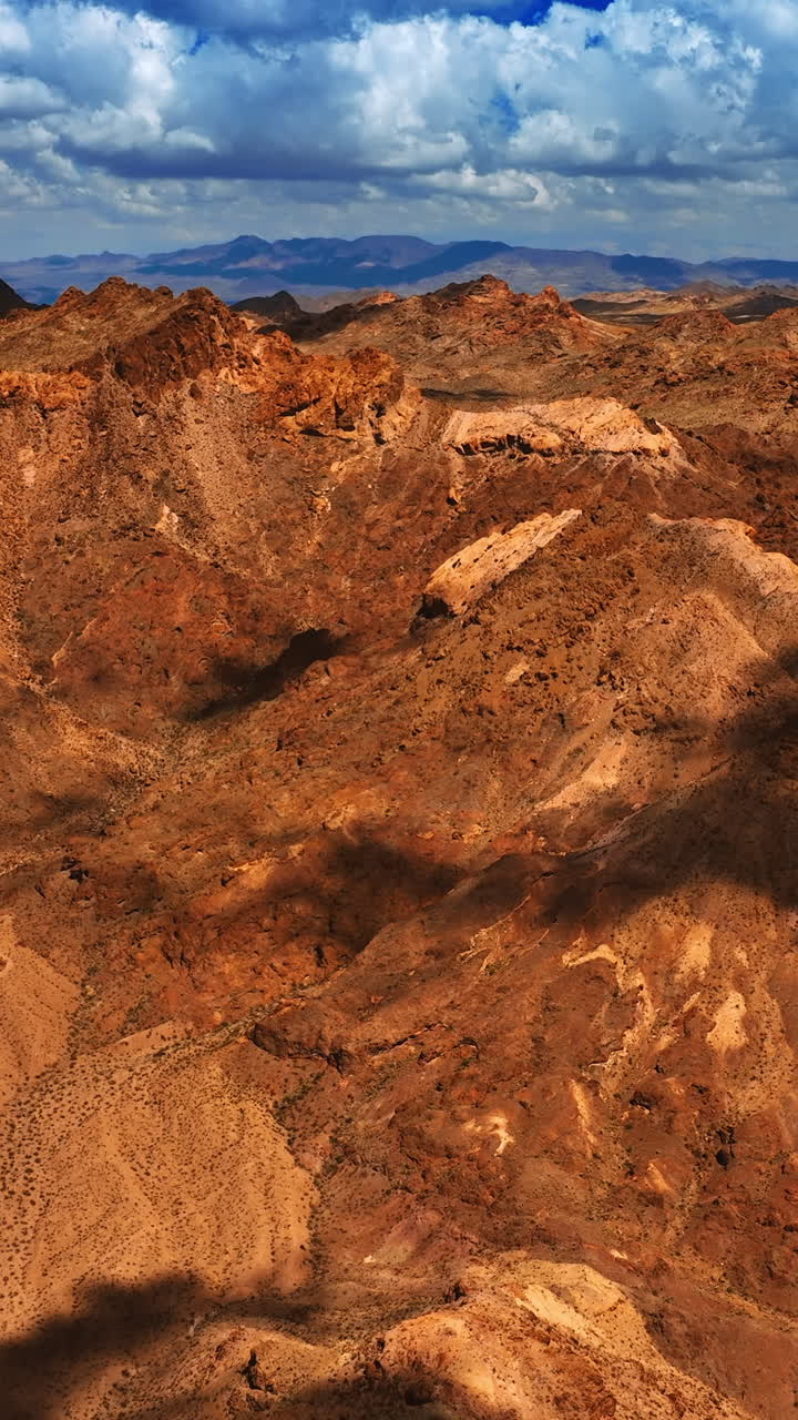 Shadows from the clouds slowly move by the tops of brown rocks. Arid lifeless mountainous landscape of Mojave desert from aerial view. Vertical video