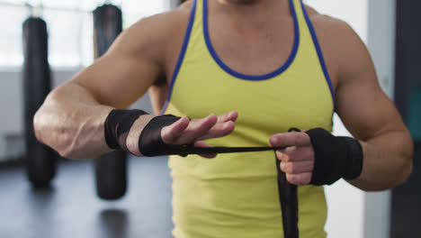 mid section of caucasian male boxer wrapping boxing tape on his hands at the gym