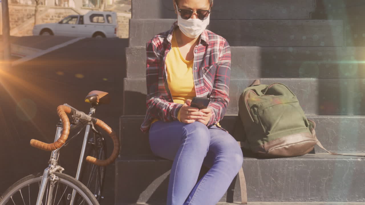 Animation of light spots over biracial woman with face mask using smartphone