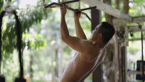 shirtless man performing pull-ups outdoors