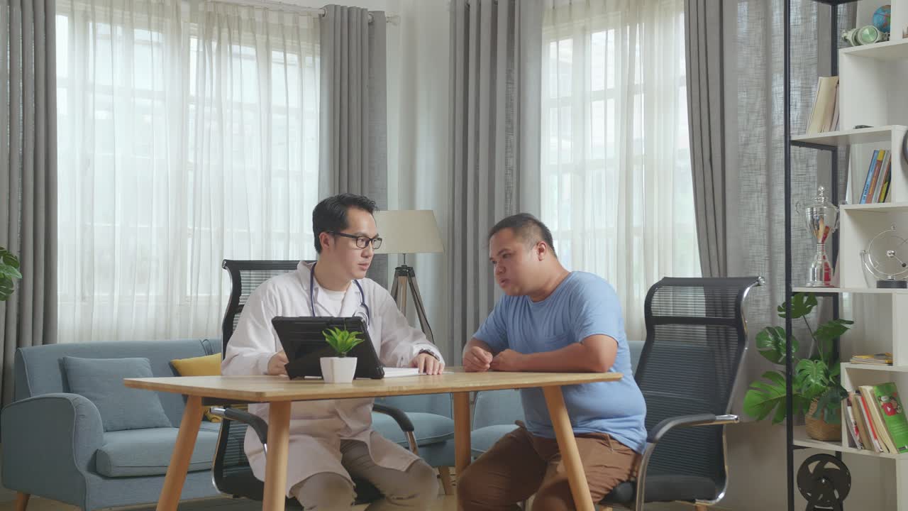클리닉에서 한 남성 환자와 함께 책상에 앉아서 태블릿에서 의료 검사 결과에 대해 논의하는 아시아 남성 의사