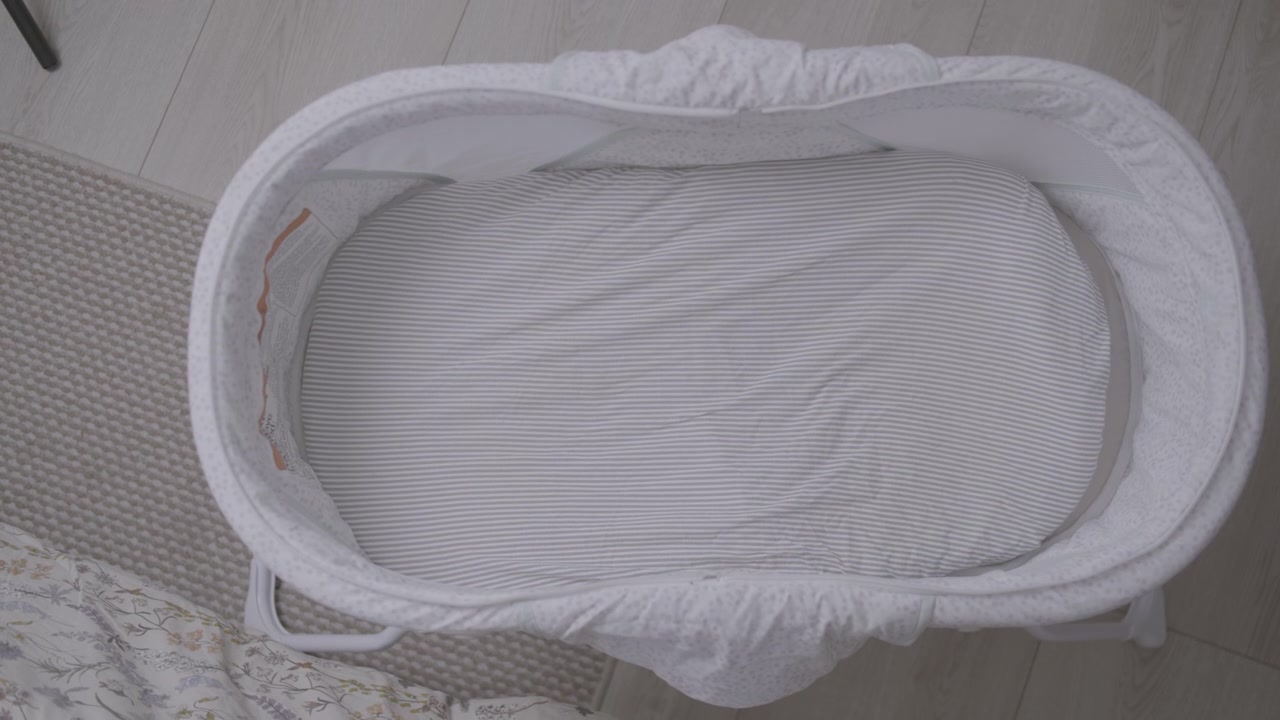 Shot from above showing the interior of an oval-shaped crib or Moses basket, completely lined with light-colored, finely striped white fabric