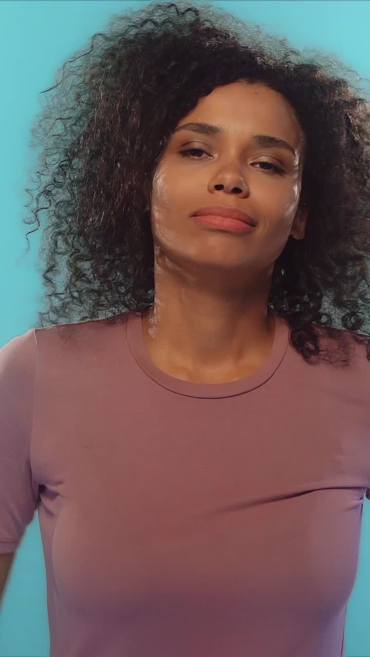 Young woman with curly hair expressing joy excitement and happiness on blue