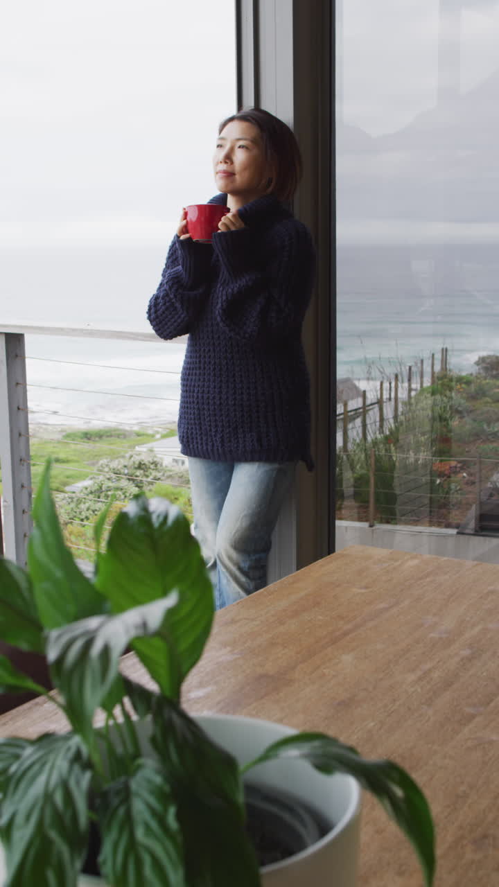 video vertical de una mujer asiática bebiendo café y pensando en la ventana sola