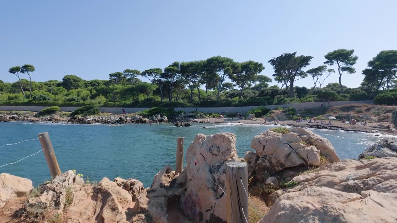 Ampia vista di una piccola caletta rocciosa lungo un sentiero costiero fiancheggiato da pini, Cap d'Antibes, Francia