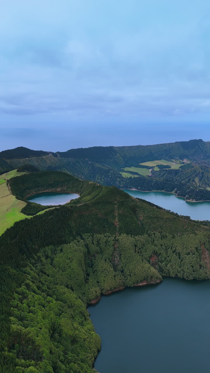 Slopes of the mountains are covered with lush green woods. Aerial perspective on the lakes located in the volcano craters. Vertical video.