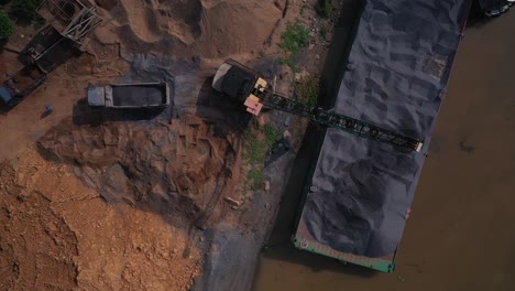 loading gravel by crane from a river barge to truck establishing shot