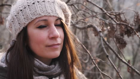 hermosa mujer con sombrero de punto y cabello castaño en el bosque mira el sol y luego sonríe a la cámara - cámara lenta, cierre