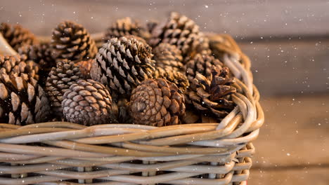 snow falling over multiple pine cones in a basket on wooden surface