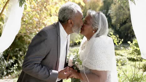 Feliz-Pareja-Birracial-Mayor-Abrazándose-Y-Sonriendo-Durante-La-Ceremonia-De-Boda-En-El-Jardín,-Cámara-Lenta