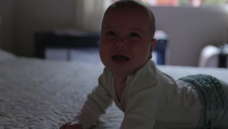 4 month old baby laying on bed looks towards camera and stops crying - close up