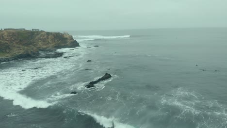 órbita aérea que revela surfistas y formaciones rocosas en un día nublado en pichilemu, chile-4k