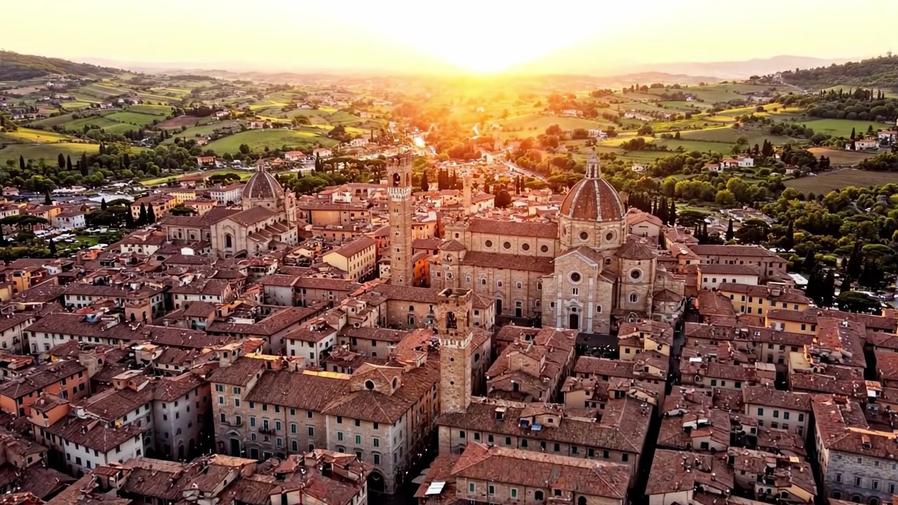 Vista aerea di architettura storica illuminata dal tramonto dorato su dolci colline e un'incantevole cittadina, che cattura l'essenza di bellezza e tranquillità senza tempo.