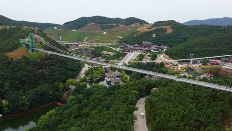 Static-aerial-drone-shot-from-a-long-suspension-glass-bridge-of-Huaxiacheng-theme-park-in-Weihai-China-with-view-of-the-beautiful-chinese-landscape-and-the-park-with-visitors-and-tourists