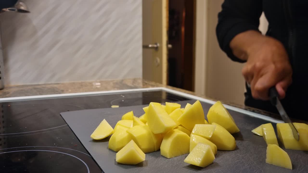 Female hands slice potatoes into bite-sized pieces, preparing a simple, healthy, and budget-friendly meal in a cozy Swiss home kitchen