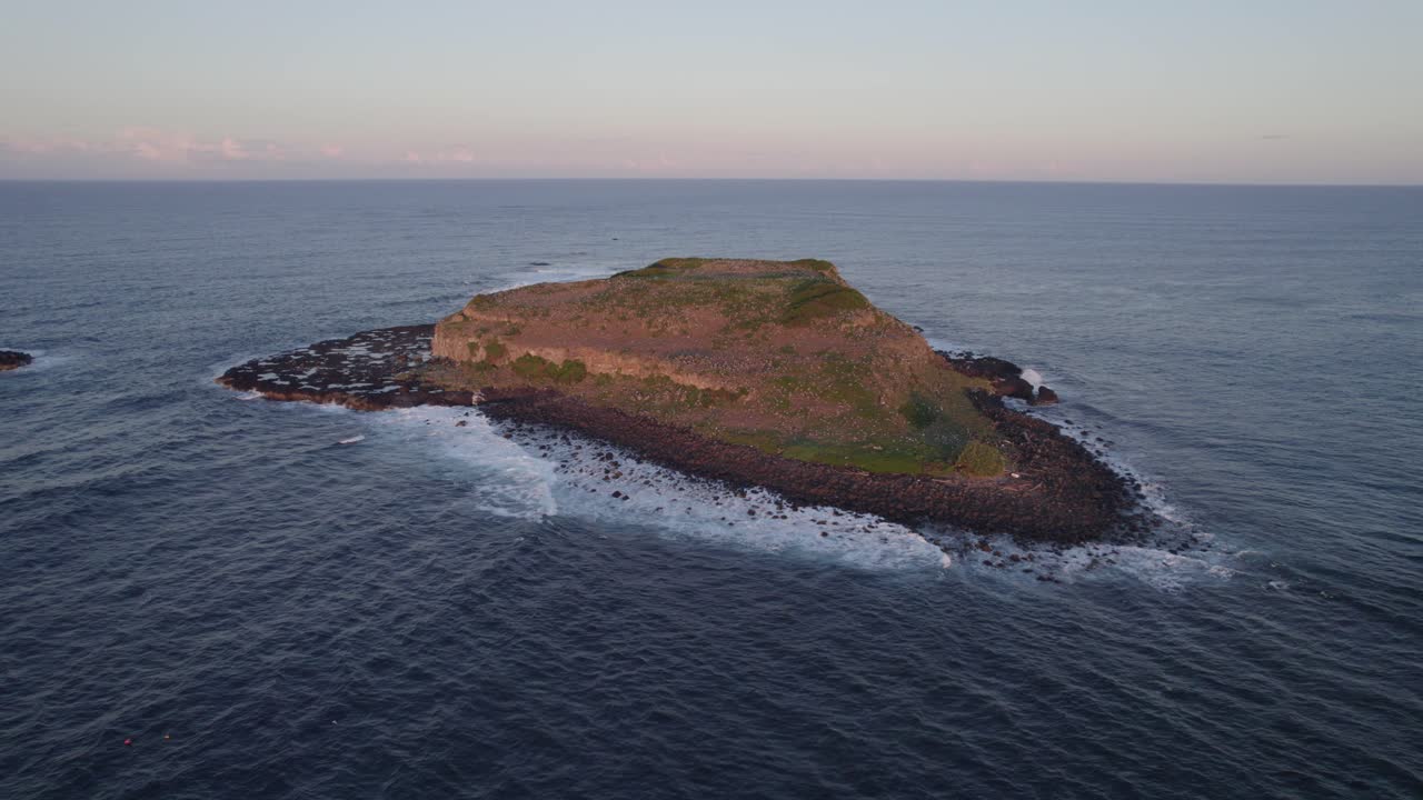 cook island off fingal headland con olas salpicando al atardecer en nueva gales del sur, australia