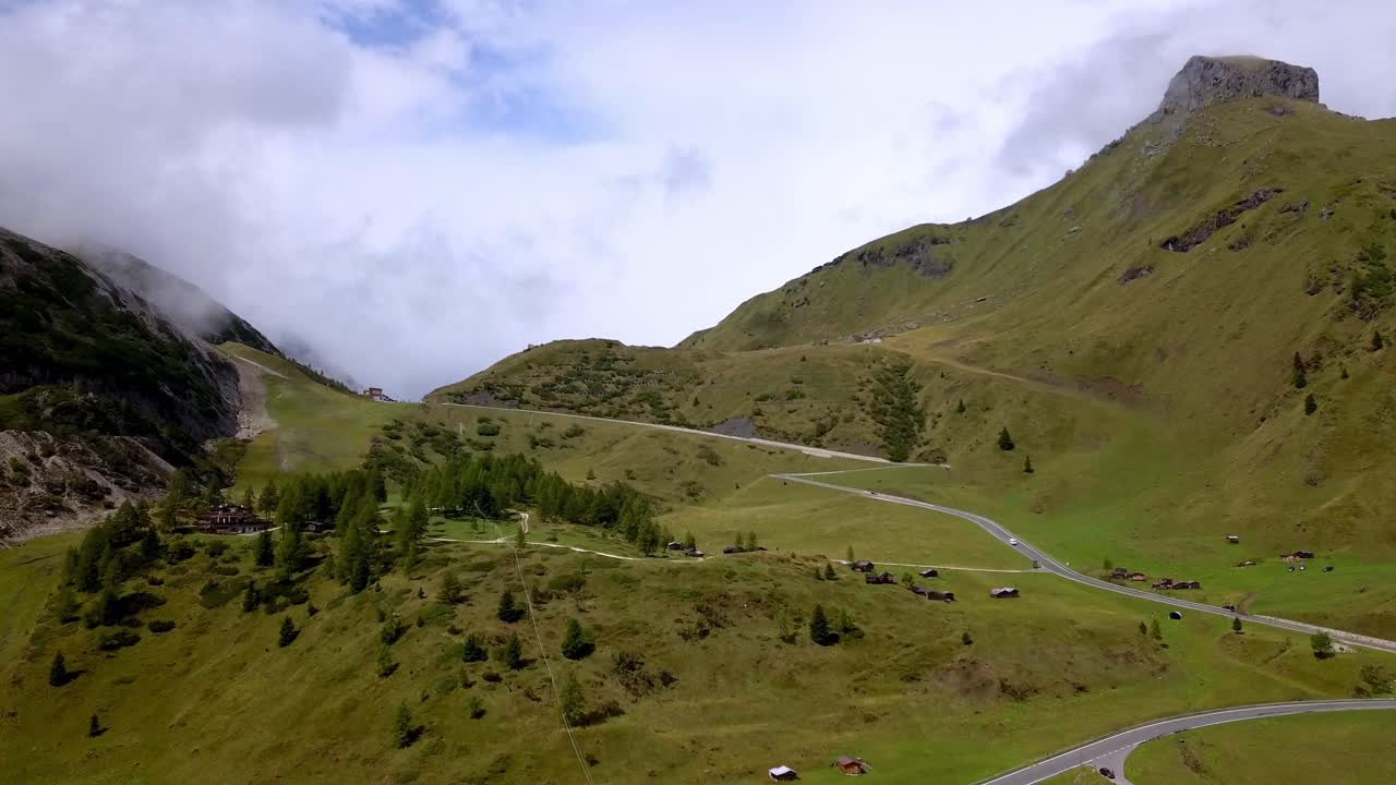 carretera sinuosa a lo largo de un paso de montaña cubierto de pastos verdes en los alpes dolomitas italianos, tiro revelador de drones
