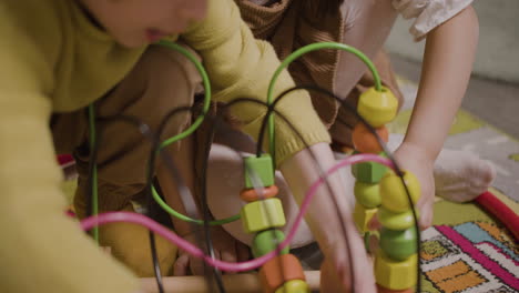 camera focuses on the hands of two children playing with with wooden pieces that move in a wire in classroom in a montessori school