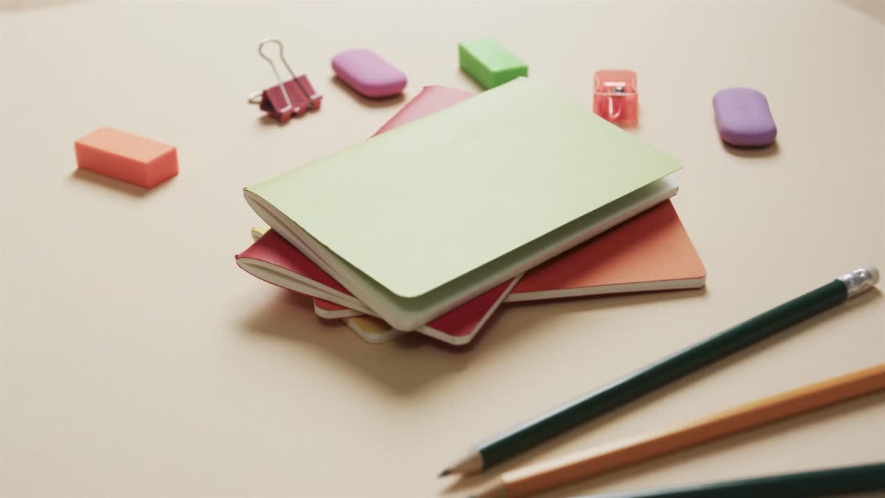 Close up of colourful notebooks with school stationery on beige background, in slow motion