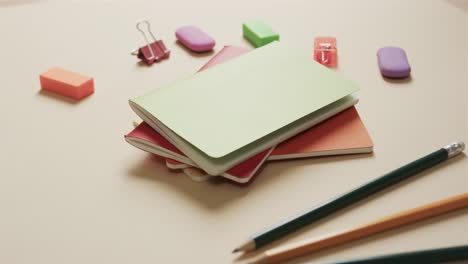 close up of colourful notebooks with school stationery on beige background, in slow motion