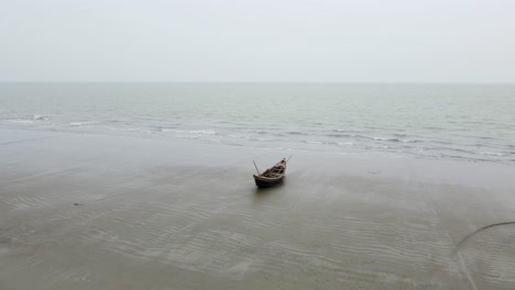 a single boat canoe rests on the shore at low tide sea beach of bangladesh in this slow drone shot