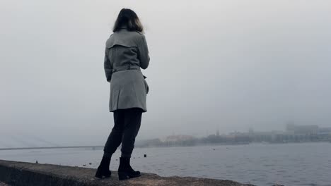 girl standing near misty river and looking how city disappears, meanwhile vaping