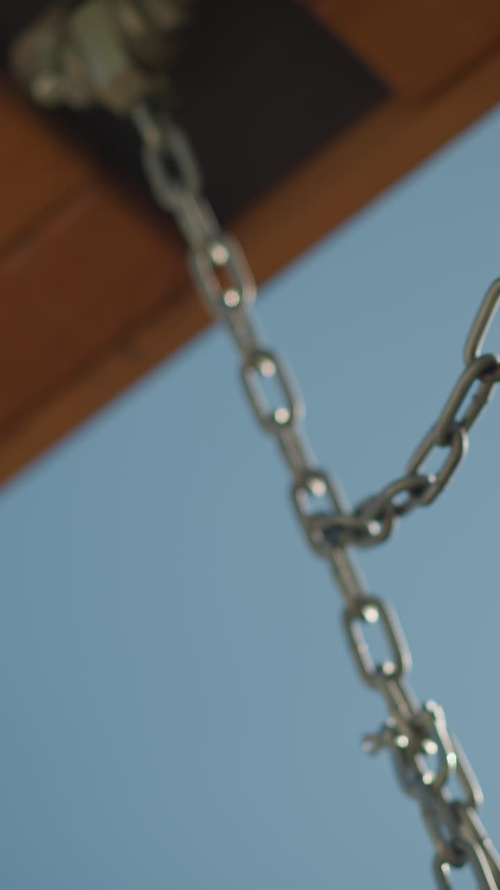 primer plano de columpio y cadena de madera en movimiento bajo un cielo claro y brillante, mostrando simplicidad y relajación en un entorno al aire libre