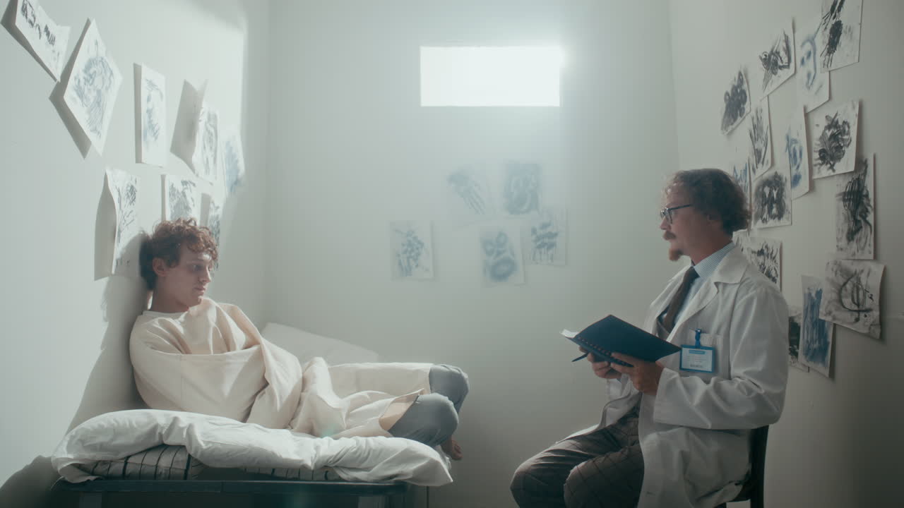 Doctor Walking in Psychiatric Room and Talking to Patient in Straightjacket