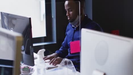 Afroamerikanischer-Mann-Mit-Gesenkter-Gesichtsmaske,-Der-Im-Modernen-Büro-Einen-Computer-Benutzt