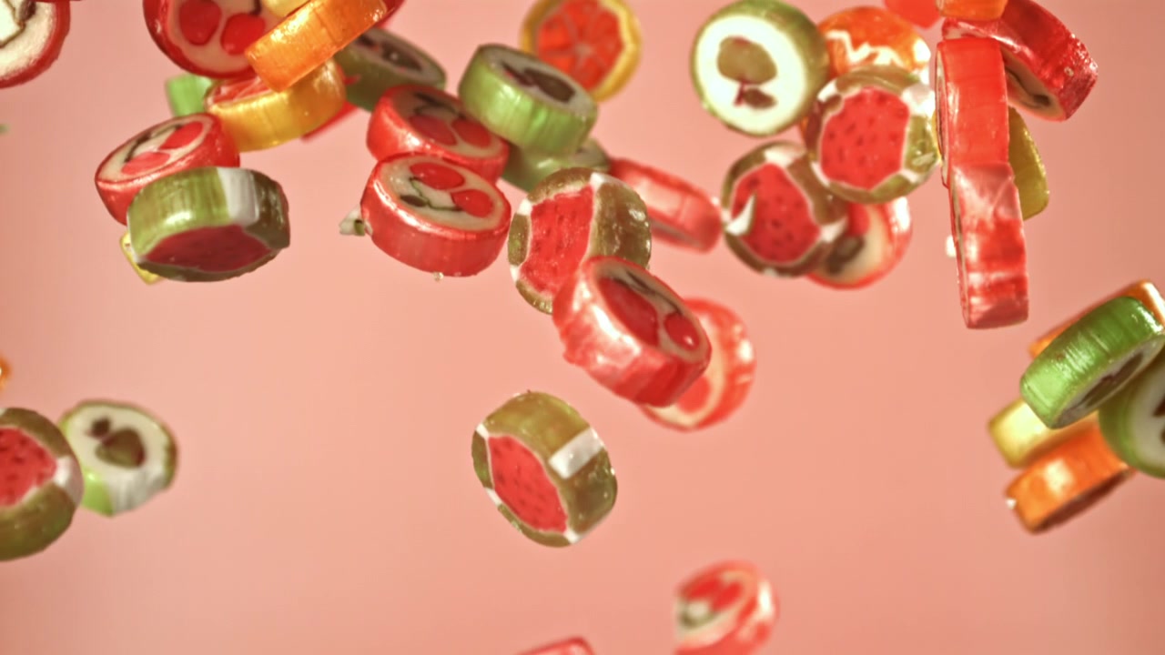 Caramelle alla frutta colorate che cadono al rallentatore su sfondo rosa