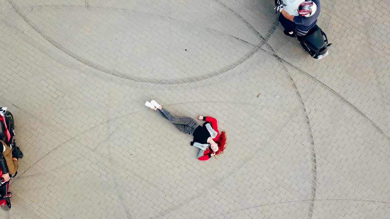 Close-up of a sexy woman with red hair and jeans lying on the road and three motorbikers riding around her. Aerial view
