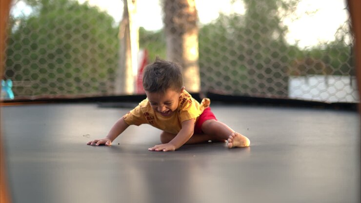 Rallentatore di un bambino latino che indossa pantaloncini rossi e una maglietta gialla, che gioca e ride su un trampolino in un pomeriggio estivo soleggiato.