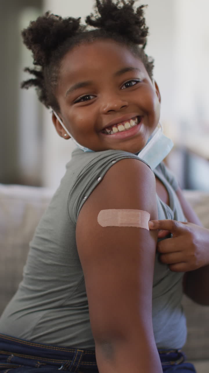 Vidéo verticale d'une jeune fille afro-américaine souriante montrant un pansement sur le bras après le vaccin contre le coronavirus
