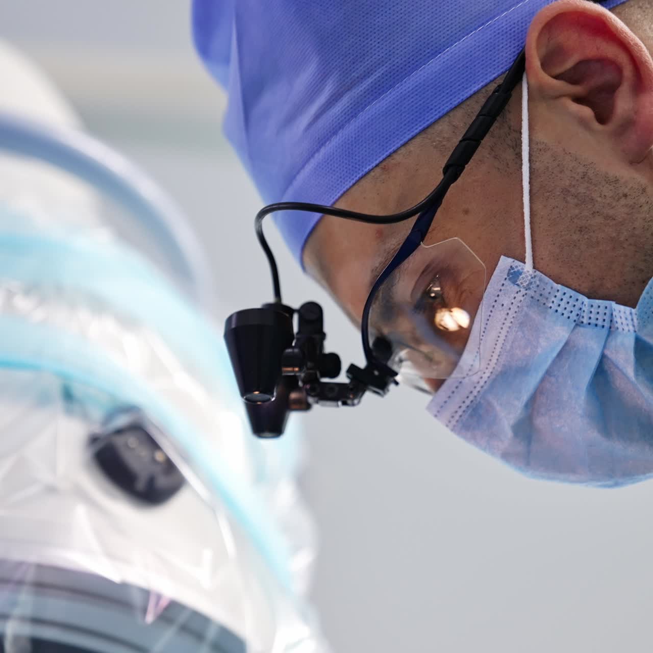 Male surgeon concentrated on his work. Light reflecting in doctor's glasses while he is operating. Side view portrait close up