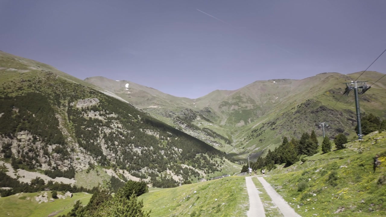 Vue panoramique imprenable sur les montagnes des Pyrénées dans la vallée de Nuria, Catalogne, par une journée d'été ensoleillée, présentant des pentes verdoyantes, un sentier de randonnée et un ciel bleu clair