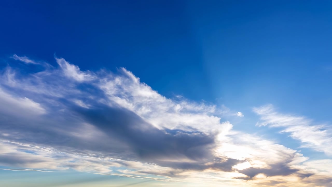 Ampia vista atmosferica di un cielo azzurro limpido con strati di nuvole soffici e un sole luminoso vicino al bordo, che crea raggi delicati e uno sfondo naturale e sereno.