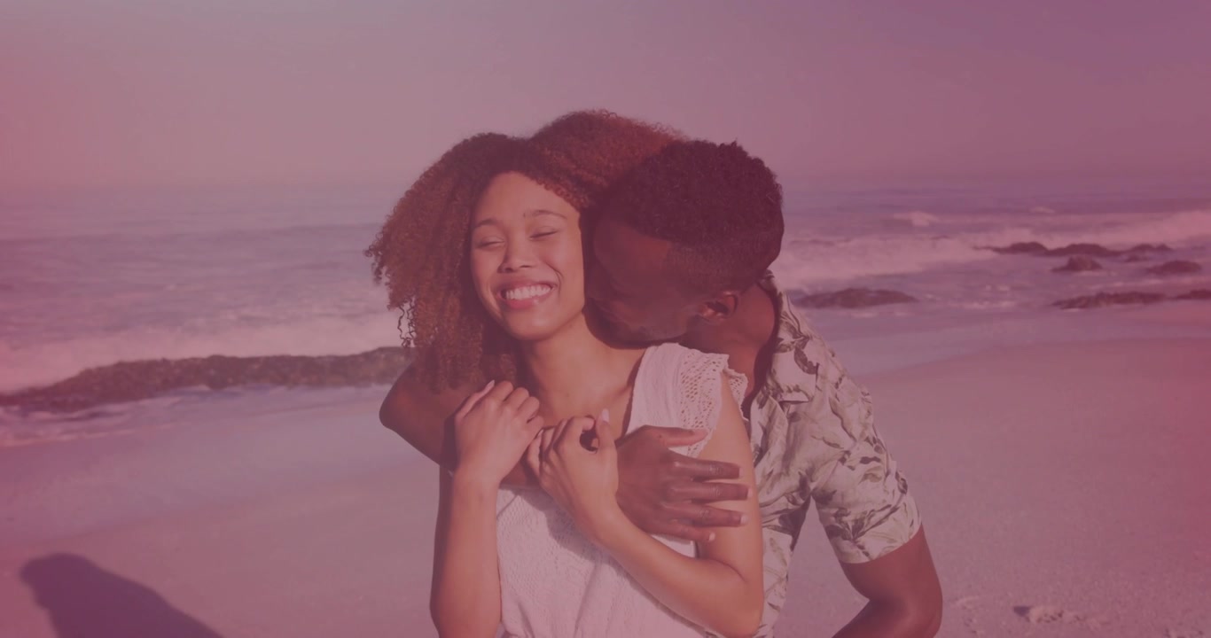 Woman posing center man coming right wrapping arms kissing neck eliciting laughter romance waves
